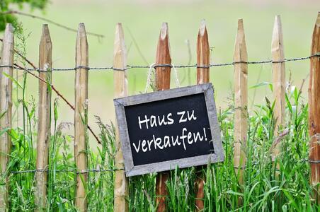 Schild „Haus zu verkaufen“ an einem Gartenzaun
